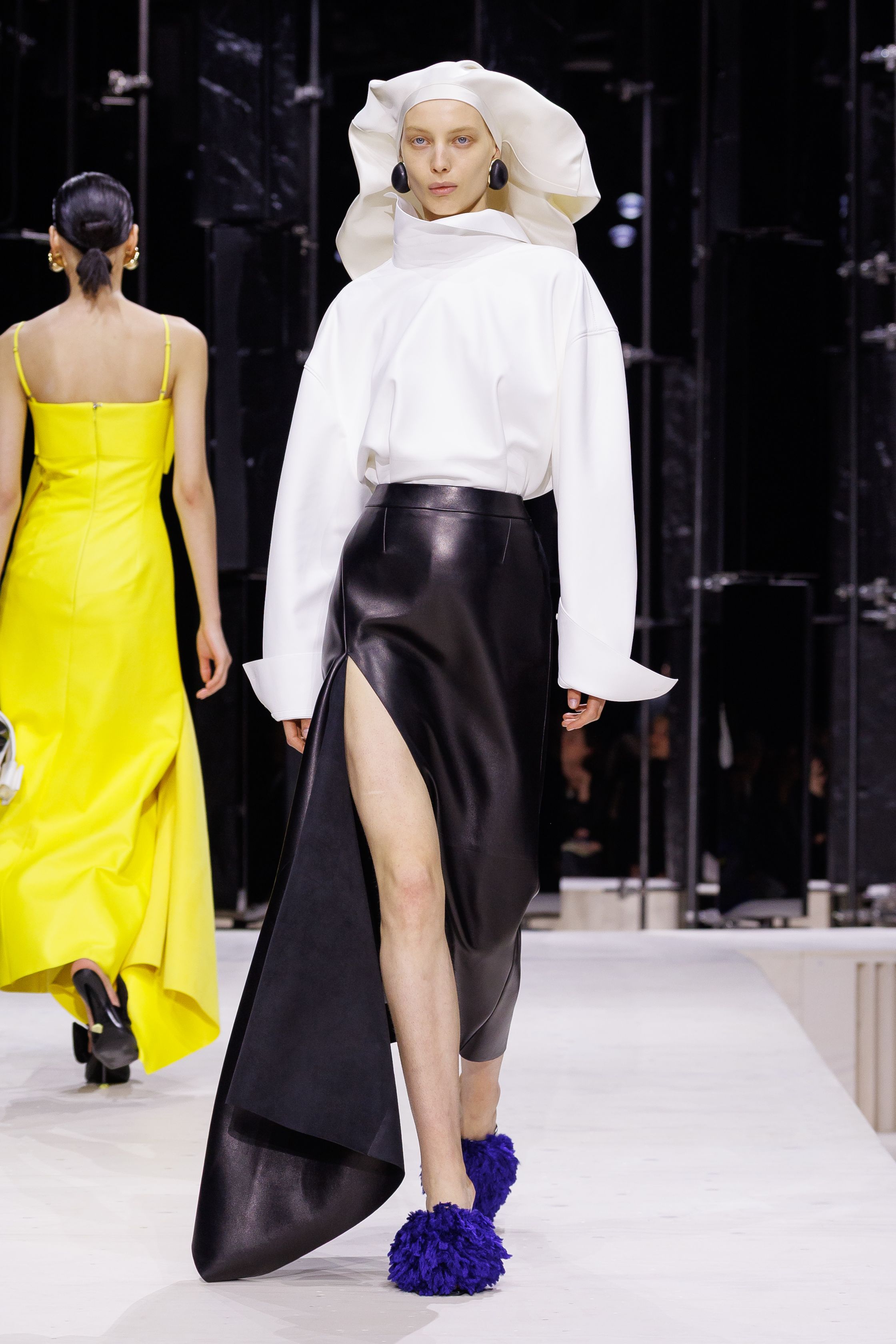 Givenchy 2026秋冬在现代建筑空间中呈现一场充满戏剧性的时装叙事：雕塑式西装、亮色斗篷、结构礼服与夸张装饰共同构建品牌标志性的高级时装气质。蓝色、红色与黄色的高饱和色彩与黑白经典形成鲜明对比，服装通过立体剪裁与夸张廓形展现出强烈视觉张力。整场系列在优雅与戏剧之间取得平衡，展现现代高级时装的力量-顽石频道趋势研究